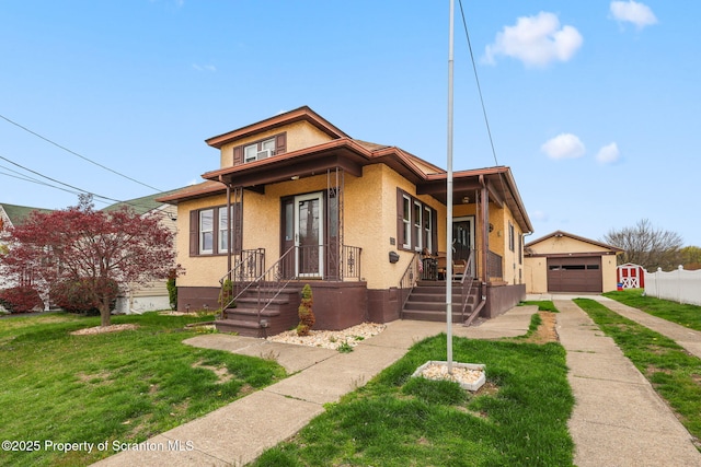 bungalow with a front lawn, driveway, an outbuilding, a garage, and stucco siding