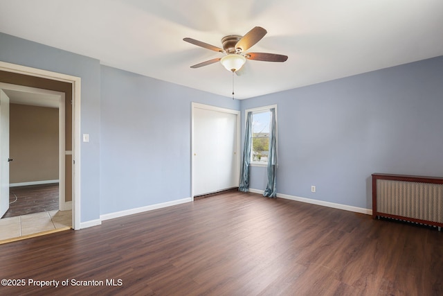 spare room with radiator, baseboards, a ceiling fan, and wood finished floors