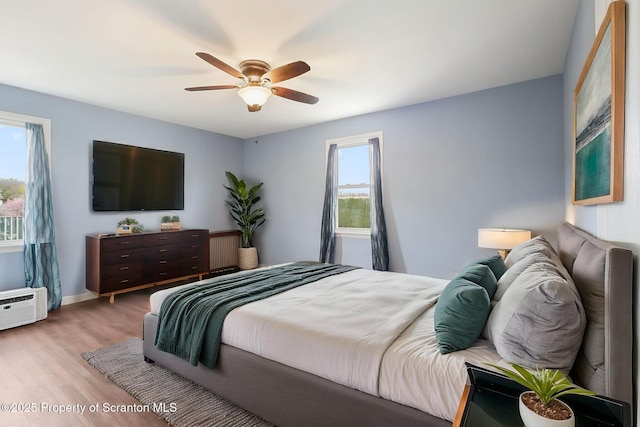 bedroom with baseboards, a ceiling fan, wood finished floors, and a wall mounted air conditioner