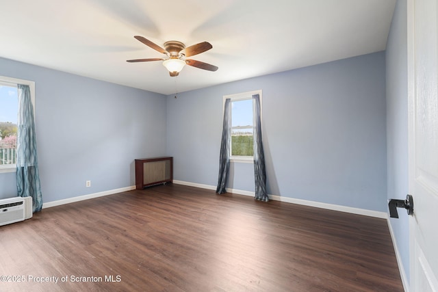 spare room featuring dark wood finished floors, a wall mounted AC, baseboards, and ceiling fan