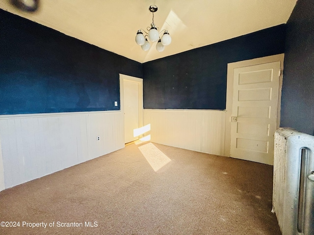 unfurnished room featuring carpet, an inviting chandelier, and radiator