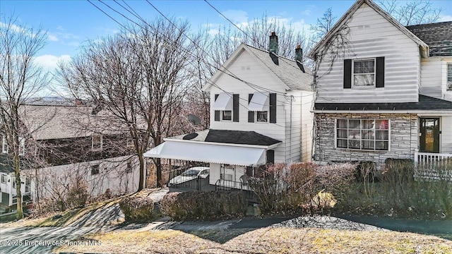 view of front of house featuring stone siding, covered porch, and a shingled roof