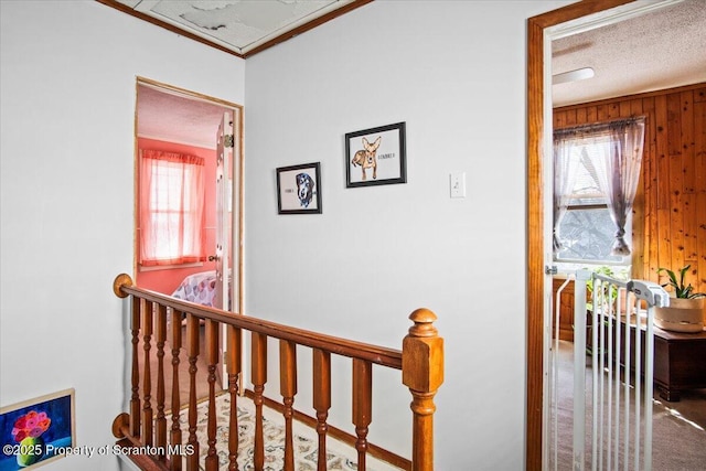 corridor with carpet floors, wood walls, a textured ceiling, crown molding, and an upstairs landing