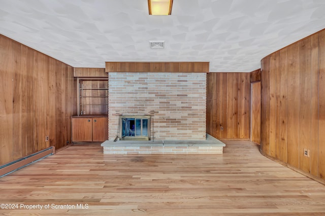 unfurnished living room featuring light hardwood / wood-style floors, wood walls, a baseboard radiator, and a brick fireplace