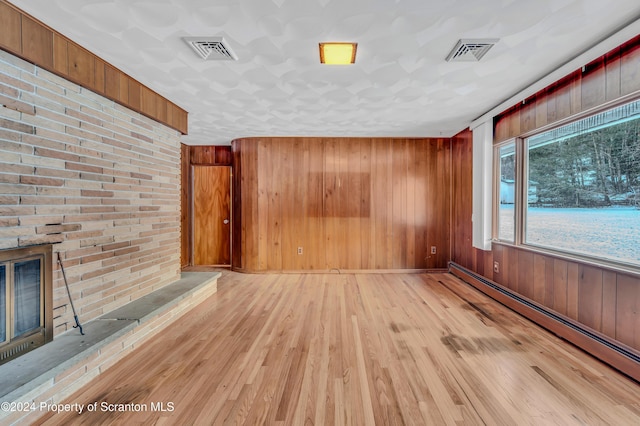 unfurnished living room with a fireplace, a baseboard radiator, light hardwood / wood-style flooring, and wood walls