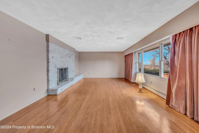 unfurnished living room with baseboard heating, a fireplace, and light wood-type flooring