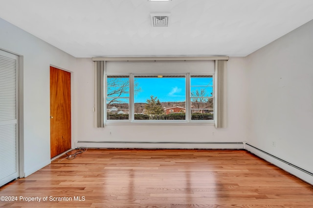 unfurnished bedroom with baseboard heating, light hardwood / wood-style flooring, and multiple closets