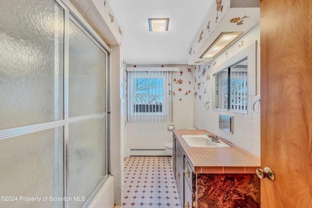 full bathroom featuring baseboard heating, toilet, shower / bath combination with glass door, vanity, and tile walls