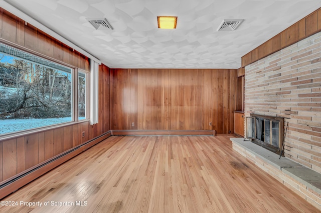 unfurnished living room featuring wood walls, a baseboard heating unit, and a brick fireplace