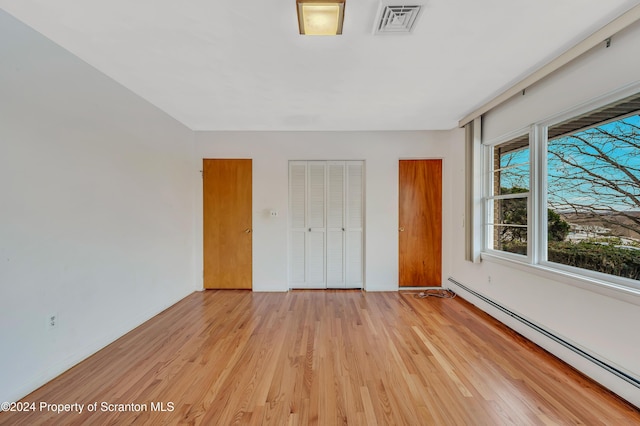 unfurnished bedroom featuring light hardwood / wood-style flooring and a baseboard heating unit