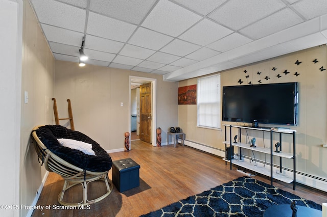 living area featuring a baseboard heating unit, a paneled ceiling, baseboards, and wood finished floors