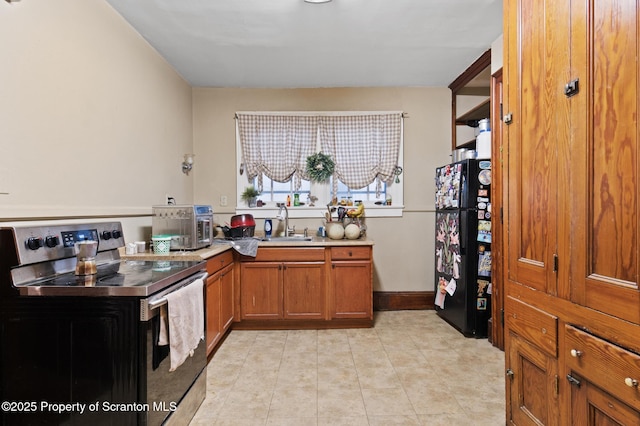 kitchen with freestanding refrigerator, a sink, light countertops, stainless steel range with electric stovetop, and brown cabinets