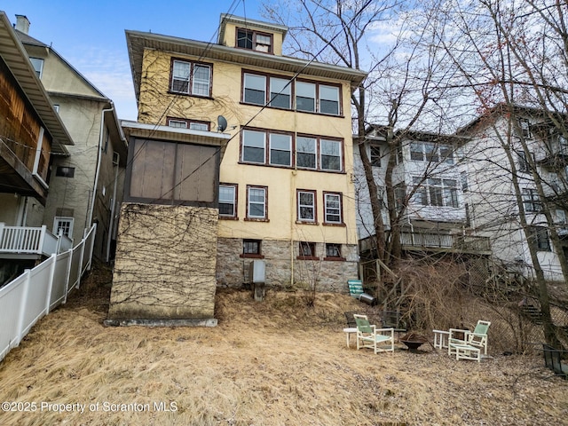 rear view of property featuring stucco siding, a fire pit, and fence