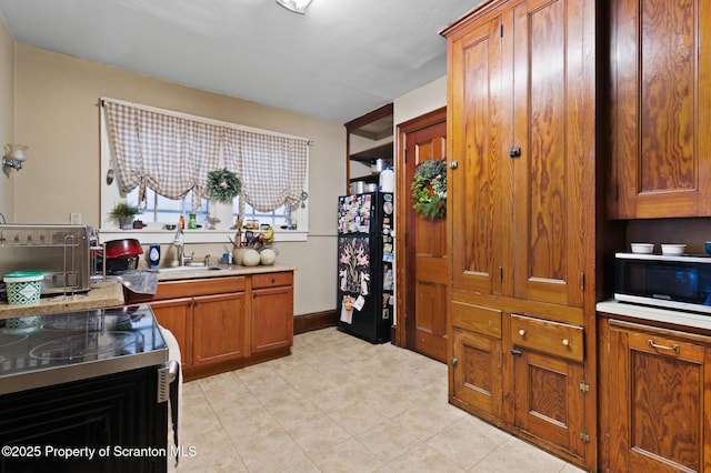 kitchen with a sink, freestanding refrigerator, brown cabinetry, a toaster, and light countertops