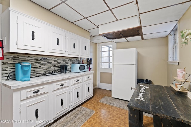 kitchen featuring a drop ceiling, decorative backsplash, white appliances, and white cabinets