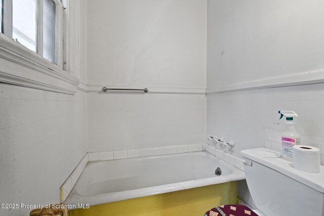 full bath with tile walls, toilet, and a bathtub