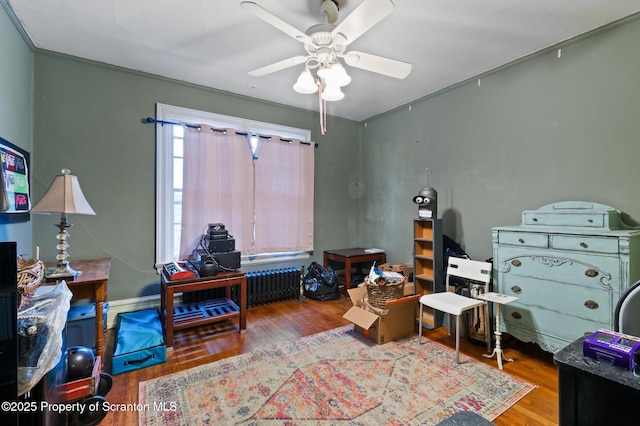 interior space featuring a ceiling fan, radiator heating unit, and wood finished floors