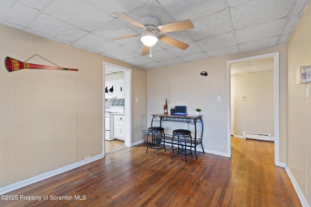 dining room with baseboards, a drop ceiling, ceiling fan, wood-type flooring, and a baseboard heating unit