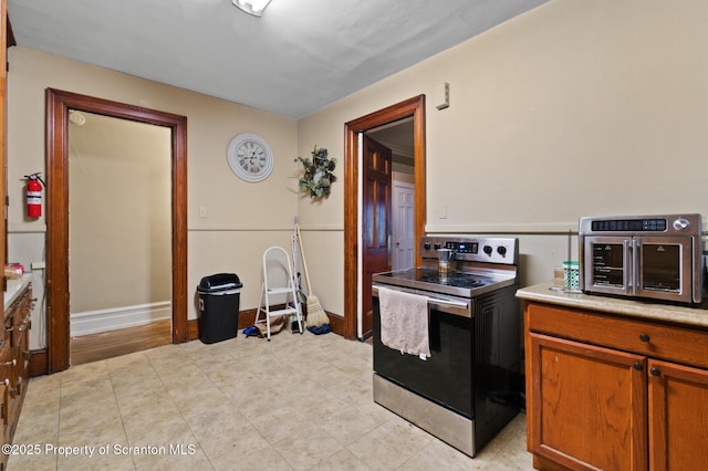 kitchen with brown cabinetry, stainless steel electric range oven, light countertops, and baseboards