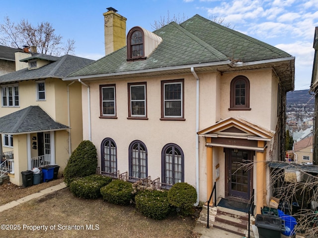 view of front of home with stucco siding, a chimney, and a shingled roof