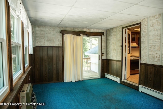 unfurnished room featuring wood walls, dark carpet, a baseboard heating unit, and a wall unit AC