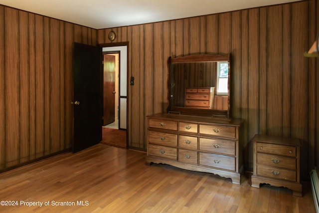 unfurnished bedroom with hardwood / wood-style flooring, wood walls, and a baseboard heating unit