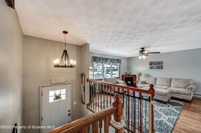 living room with wood-type flooring, a baseboard heating unit, and ceiling fan with notable chandelier