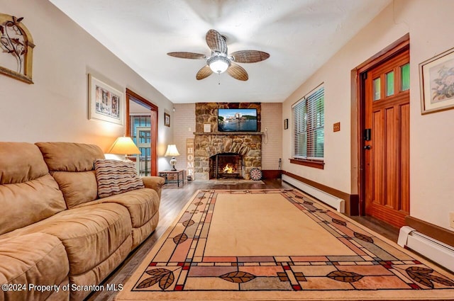 living room featuring wood-type flooring, a stone fireplace, baseboard heating, and ceiling fan