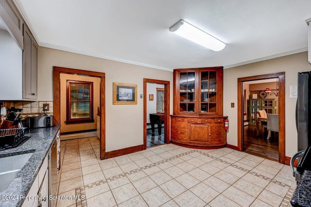 kitchen with sink, a baseboard heating unit, backsplash, light tile patterned floors, and ornamental molding