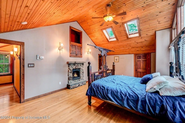 bedroom featuring a stone fireplace, ceiling fan, vaulted ceiling with skylight, and wood ceiling