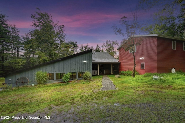 back house at dusk featuring a sunroom and a yard