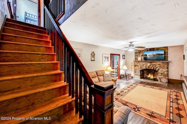 living room featuring a stone fireplace, ceiling fan, hardwood / wood-style floors, and a textured ceiling