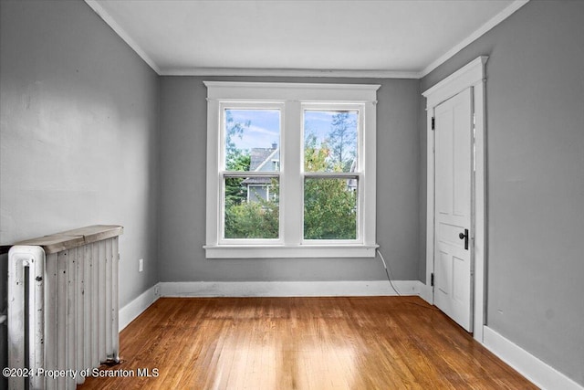 empty room featuring radiator heating unit, a wealth of natural light, crown molding, and wood-type flooring