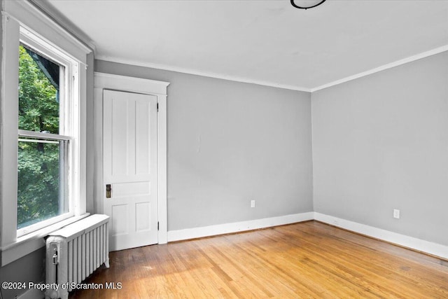 empty room with hardwood / wood-style flooring, crown molding, and radiator