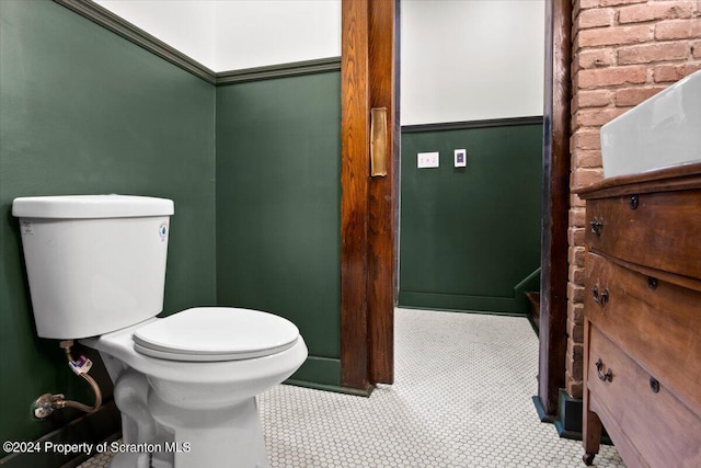 bathroom featuring tile patterned floors, toilet, and brick wall