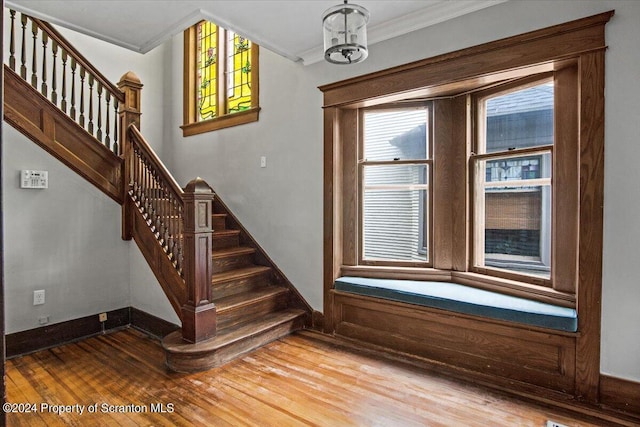 stairway with wood-type flooring, crown molding, and an inviting chandelier