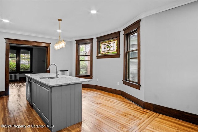 kitchen with gray cabinetry, radiator, sink, an island with sink, and pendant lighting