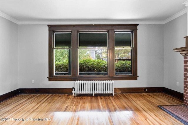 empty room featuring a fireplace, hardwood / wood-style floors, radiator, and crown molding