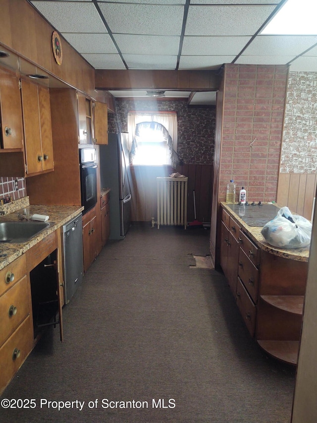 kitchen featuring brown cabinetry, radiator heating unit, stainless steel appliances, dark colored carpet, and a paneled ceiling