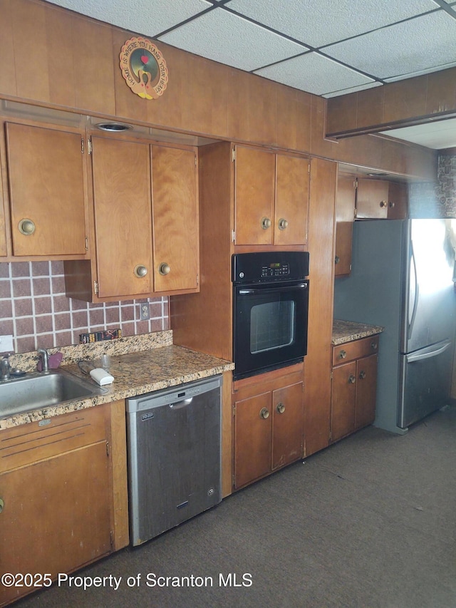 kitchen with brown cabinets, freestanding refrigerator, black oven, and dishwashing machine