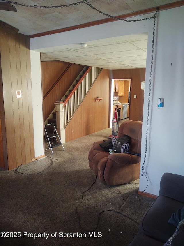 living room featuring carpet flooring, wooden walls, and stairs