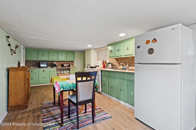 kitchen with sink, light hardwood / wood-style floors, green cabinetry, and white refrigerator