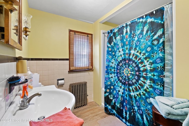 bathroom with radiator, hardwood / wood-style floors, tile walls, and sink