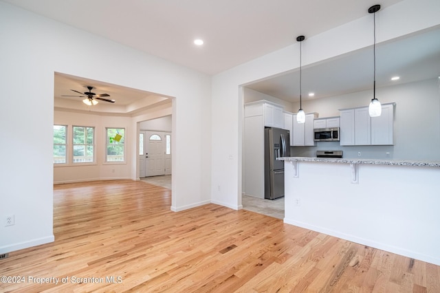 kitchen featuring white cabinetry, ceiling fan, hanging light fixtures, stainless steel appliances, and light hardwood / wood-style flooring