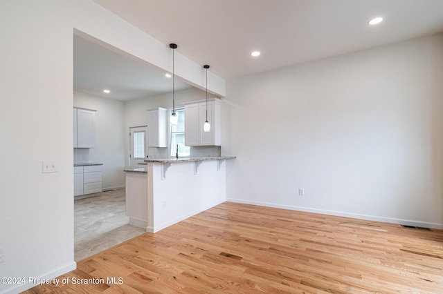 kitchen with kitchen peninsula, a kitchen breakfast bar, pendant lighting, white cabinets, and light hardwood / wood-style floors