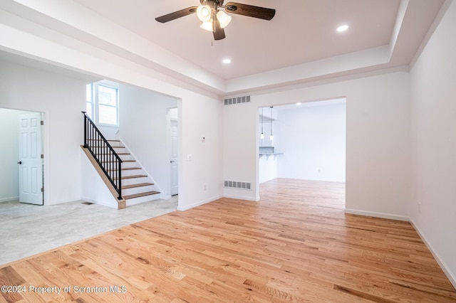 spare room with a tray ceiling, light hardwood / wood-style flooring, and ceiling fan