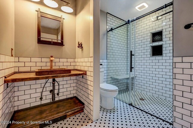 bathroom with a shower with door, sink, tile patterned flooring, toilet, and tile walls