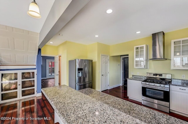 kitchen featuring dark wood-type flooring, white cabinets, wall chimney range hood, light stone countertops, and stainless steel appliances