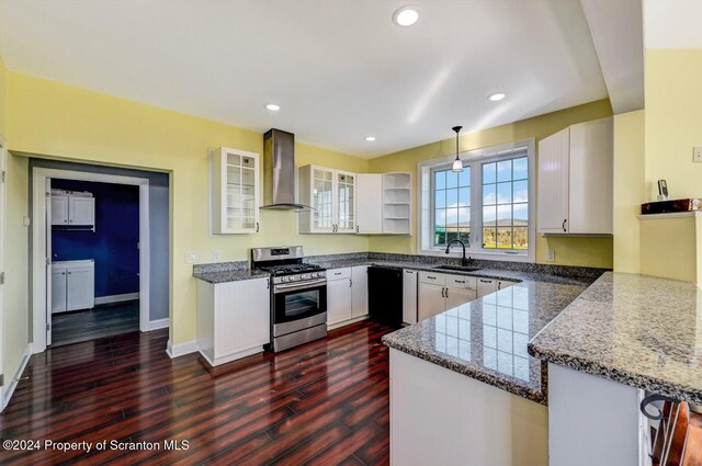 kitchen featuring stainless steel gas stove, wall chimney range hood, kitchen peninsula, decorative light fixtures, and white cabinets