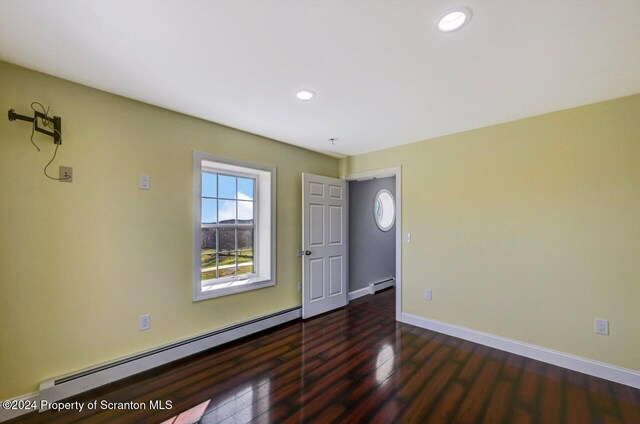 unfurnished room with dark wood-type flooring and a baseboard heating unit